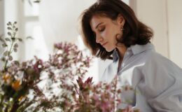 woman in white blazer looking at pink flowers