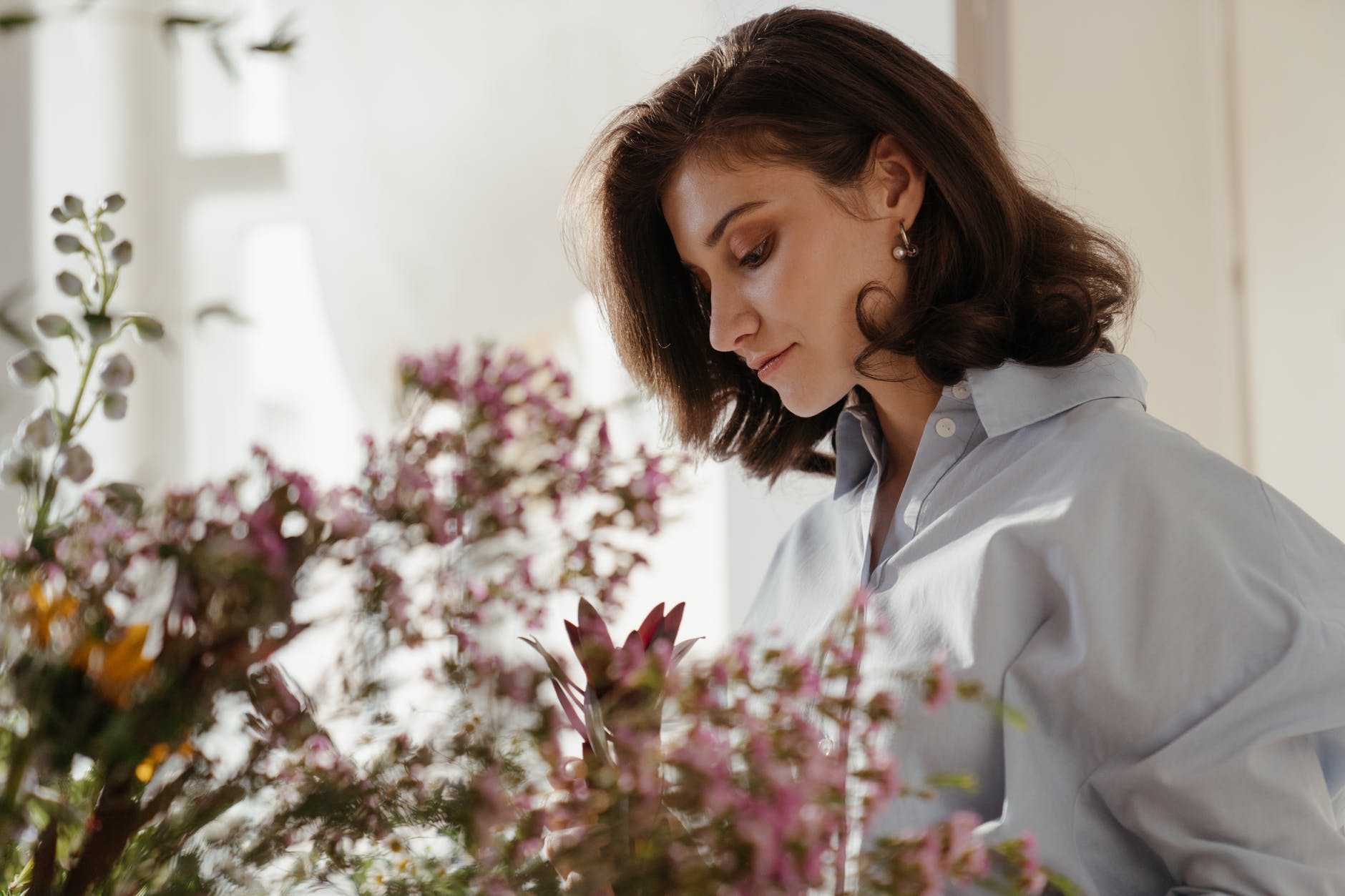 woman in white blazer looking at pink flowers