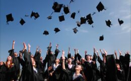 newly graduated people wearing black academy gowns throwing hats up in the air