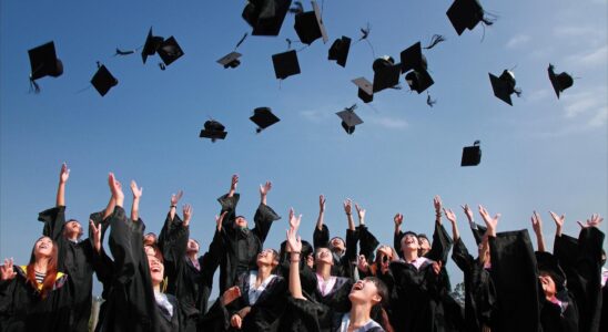 newly graduated people wearing black academy gowns throwing hats up in the air