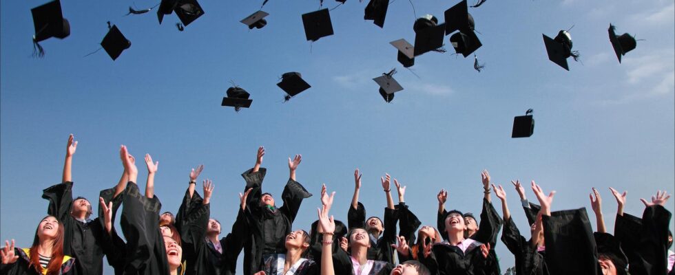 newly graduated people wearing black academy gowns throwing hats up in the air